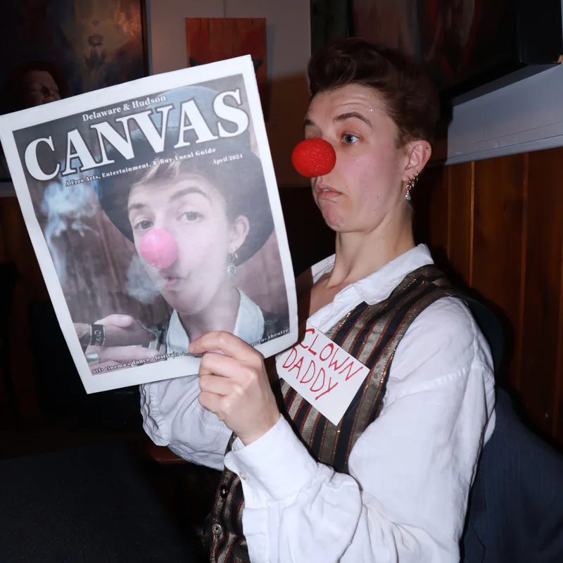 Ellie J in a red clown nose holding up a newspaper with her own photo on the cover