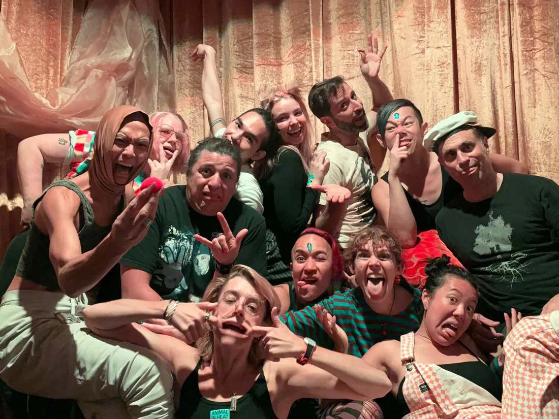 A workshop group in red clown noses piled together laughing with Ellie J on a stage